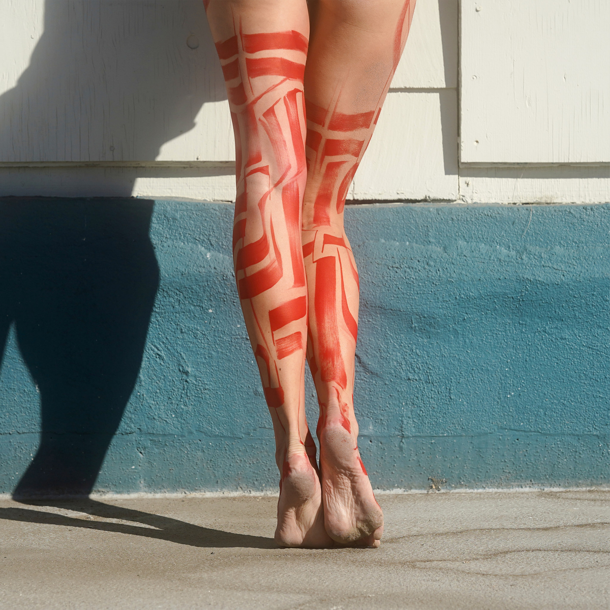 Red Boots photograph by VEFA Gallery: legs covered in red abstract body paint against a white and teal wall.